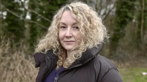 A picture of Samantha Jenkins looking into the camera. She is standing outside with trees behind here.