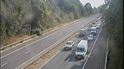 A slightly blurred traffic camera showing stationary vehicles on one side of the motorway. 