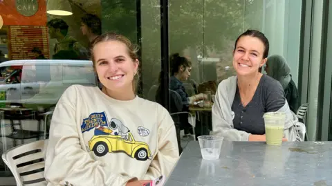 BBC Lola Nordlinger (left) and Keely Ganong (right) sit in a coffee shop.