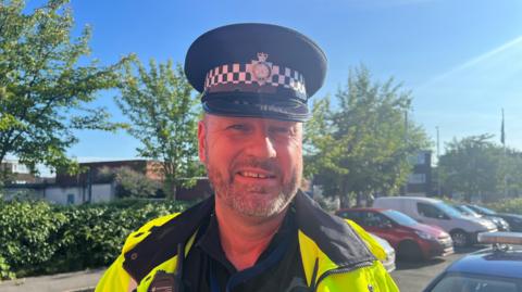 Inspector Greg Laidlaw, wearing a police uniform of high vis jacket and black cap, smiling at the camera