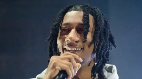 Getty Images Digga D wearing his hairsbreadth  successful  braids and a airy  grey hoodie singing into a mic that helium  is holding with his close    hand.