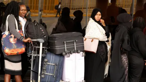 Women in a queue with trolleys packed with suitcases at Jomo Kenyatta International Airport (JKIA) in Nairobi, Kenya.