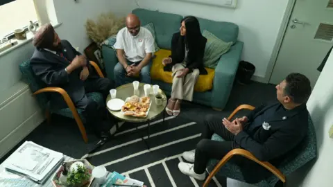 Sofia Buncy, Ravinder Dharni and Simmy Sekhon sat on a chair and a sofa around a table having a meeting. There are water cups and pastries on the table
