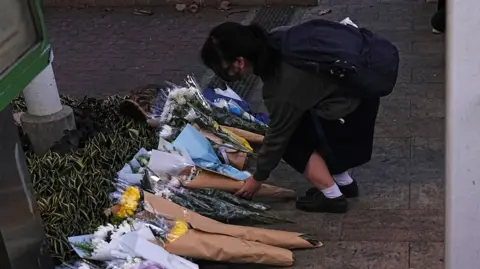 Reuters A student places a flower bouquet at the scene after a deadly fire at the Wang Fuk Court housing complex.