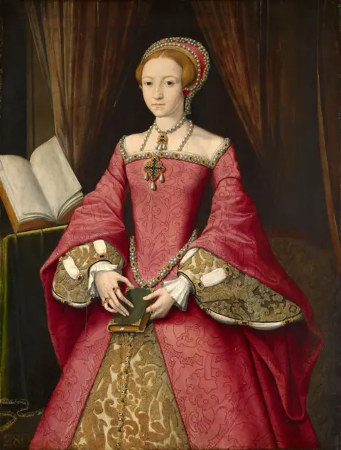 Royal Collection Enterprises Limited 2026 | Royal Collection Trust A painting of young Elizabeth I in a red and gold dress. She is holding a book and there is a larger, open book on the left-hand side. 