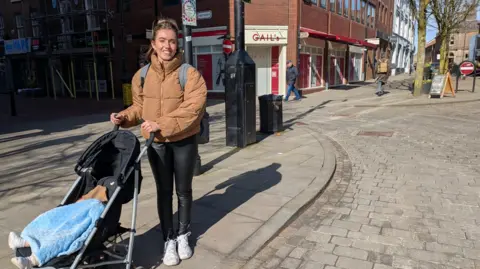 Stephanie Lamb con un niño pequeño en una silla de paseo en las afueras de Gail antes de que esté abierto