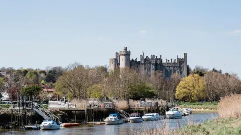 Several boats moored on a river. There is a stone castle in the background.
