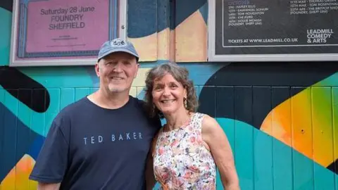 A man and woman stood in front of a painted wooden doorway