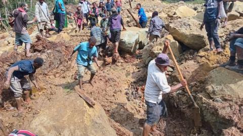 Villagers clamber over the landslide and use shovels to break up the earth