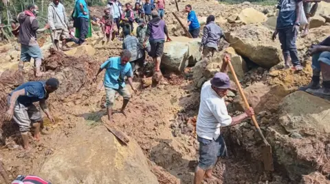 UN INTERNATIONAL ORGANIZATION FOR MIGRATION Villagers clamber over the landslide and use shovels to break up the earth