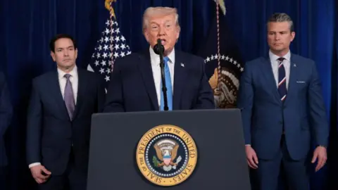 President Donald Trump speaks behind a podium with Marco Rubio on his left and Pete Hegseth on his right.