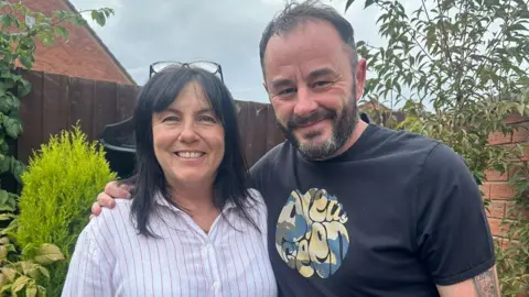 Stuart McCullagh A dark-haired woman in a white and pink striped shirt and a man with his arm around her wearing a black T-shirt