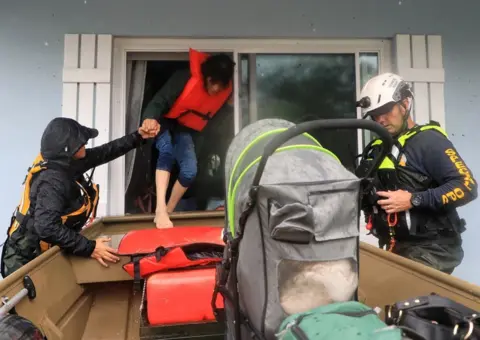 Nadia Zomorodian / Daytona Beach News-Journal Volusia Sheriff's Special Ops team members in rescue gear help a resident in a life vest into a boat out their window in South Daytona, Florida, U.S., October 10, 2024.