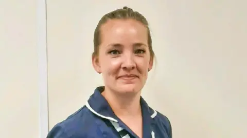 Naomi House & Jacksplace A woman in a blue and white clinician uniform. She has a white lanyard around her neck. 
