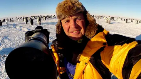 Nature photographer Doug Allan with penguins behind him