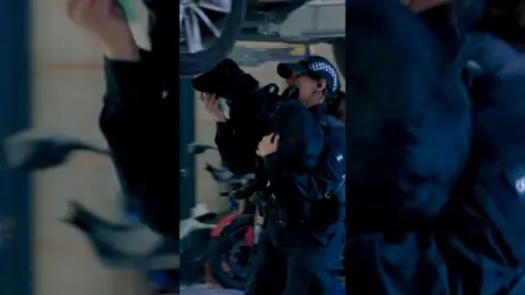A black dog being carried by a female police officer under an elevated car