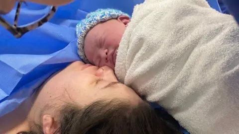 Nathan Barnes A mother and newborn baby lying face to face under hospital blankets.