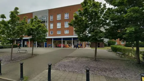 Google A convenient store, with trees and several benches in front of it.