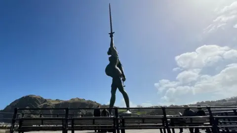 The statue of Verity stands on the harbour in Ilfracombe with benches in the foreground