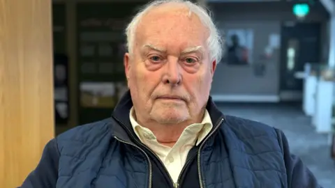 A man with white hair and a navy padded jacket 
