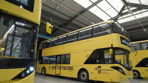 PA Media A row of yellow Manchester buses, with Bee Network written on the side of each one.