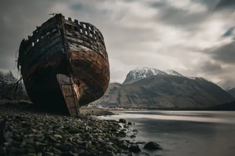 Jon Simmonds A shipwreck on the bank of a loch with a mountain in the background
