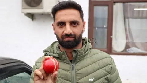 Auqib Nabi Dar poses with a red cricket ball in Baramulla, Jammu and Kashmir, India, on March 18, 2026. Auqib Nabi Dar is an Indian cricketer who plays as a right-arm medium bowler. He represents Jammu & Kashmir in domestic cricket and Delhi Capitals in the Indian Premier League. (Photo by Nasir Kachroo/NurPhoto via Getty Images)