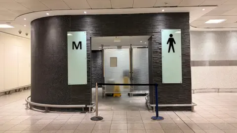 The entrance of a men's toilet which is blocked off.