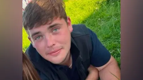 Robert Kissack, a young man with light brown hair and blue eyes smiles.