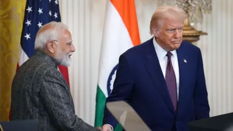 India Prime Minister Narendra Modi shakes hands with President Donald Trump at the White House in February during a press conference. Behind the two men are the flags of India and the US. Modi stands in profile while Trump is looking forward.