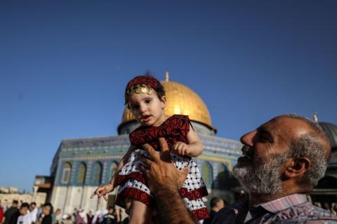 Man carrying little girl dressed in traditional Palestinian attire