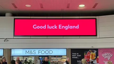 Gatwick Airport A large red electronic sign at Gatwick Airport, reading Good Luck England in white text