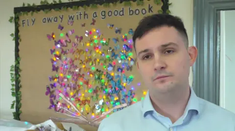 Ellis Jenkins of Sunnybank nursery looking at the camera, in front of a colourful mural with the logo 'Fly away with a good book'