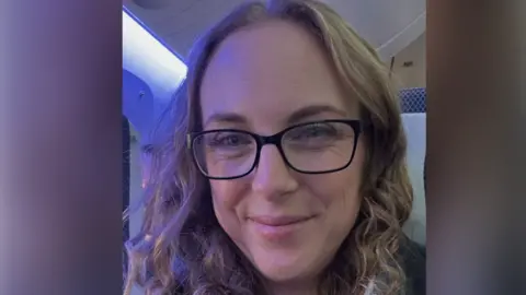 Laura Minor Laura Minor., a woman with wavy hair and glasses is smiling at the camera