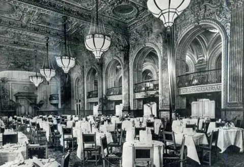 Grand Hotel A black and white photo of the ballroom. Chairs surround dozens of tables set with white linen in a huge, ornate room, set with tall arches in the background and decorative ceiling