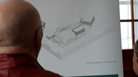 A bald man looking away at at computer generated plan of what the site could look like