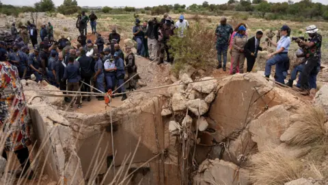 Reuters Community members watch as Senzo Mchunu, South African police minister, inspects outside the mineshaft where it is estimated that hundreds of illegal miners are believed to be hiding underground.