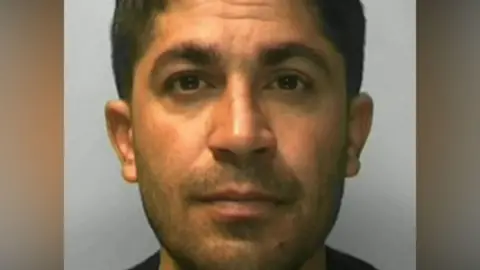 Sussex Police A police custody image shows Sherzad Salih, with short dark hair and stubble, looking at the camera. 