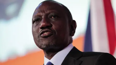 William Ruto, in a black suit, white shirt and blue tie