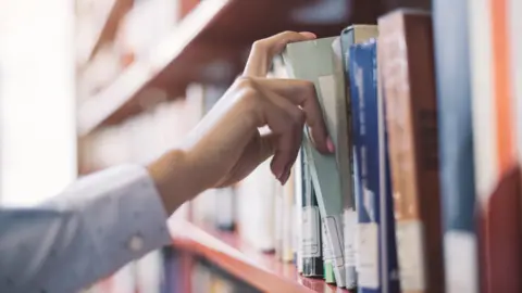 Getty Images A hand picking a book from a bookshelf