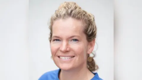 Smartphone Free Childhood Charlotte Carson is wearing a blue top, she had long blonde brown hair. She has golden ear rings in her ears. The background is white. 