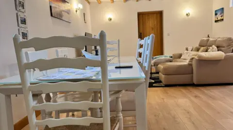 St Michael's Hospice A table with a glass surface and matching chairs, painted white, and a sofa with cushions in the background.