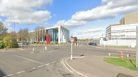 Google A Google Street View of a junction between a service road and a main road. Across the road a modern sign on a red horizontal block marks the entrance to Slough Trading Estate.