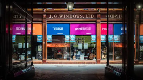 The multi-coloured shop front of J.G Windows. Musical instruments can be seen through the windows.