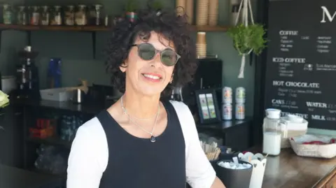 Getty Images Zayna Omer standing in her coffee shop, wearing sunglasses and smiling.