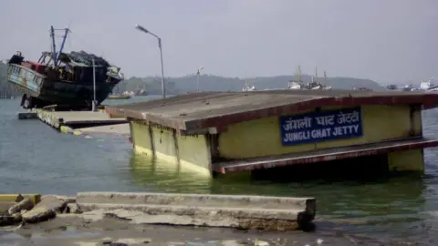 Getty Images Sebuah gambar yang diambil pada 28 Desember 2004 menunjukkan dermaga pantai yang banjir di Port Blair, ibu kota negara bagian Kepulauan Andaman dan Nikobar di tenggara India. Gelombang besar yang dipicu oleh gempa bumi tanggal 26 Desember, menewaskan sedikitnya 4.000 orang di pulau-pulau tersebut dan menyebabkan ribuan orang hilang dan tak terhitung jumlahnya kehilangan tempat tinggal di India sementara jumlah korban tewas mencapai 8.500 akibat tsunami yang menghantam pantai-pantai yang tidak terlindungi di seluruh Asia. 