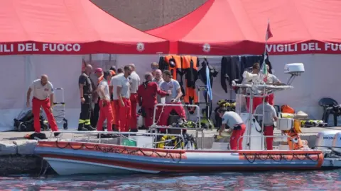 PA Media Group of fire brigade diving team in uniform next to a rescue boat, with emergency tents in the background