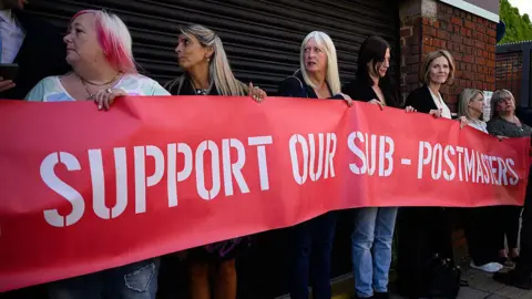 A group of those affected by the Horizon IT issue hold a banner, as the first volume of a report from the Post Office Horizon IT Inquiry is announced at The Kia Oval