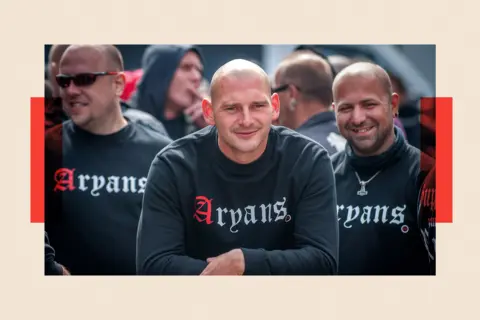 Getty Images Three men wearing black jumpers that say "Aryans" on the front