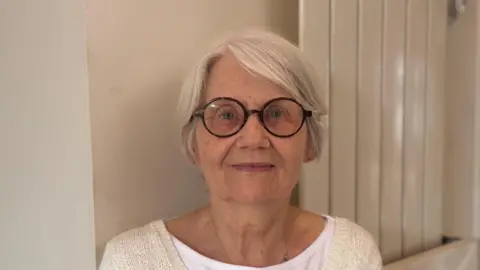 George King/BBC A head and shoulders image of Fran Tuck. She is wearing glasses and a cream cardigan over a white T-shirt. She is looking into the camera.